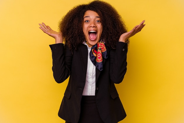 Young African American air hostess isolated on yellow wall celebrating a victory or success, he is surprised and shocked.