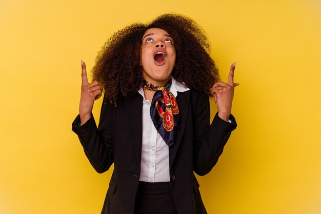 Young African American air hostess isolated on yellow wall pointing upside with opened mouth.