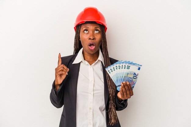 Молодой афро-американский архитектор женщина, держащая счета, изолированные на белом фоне, указывая вверх с открытым ртом.