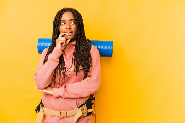 Young african american backpacker woman isolated relaxed thinking about something looking at a copy space.