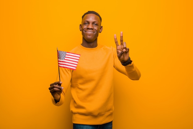 Young african american black man against orange wall holding an usa flag