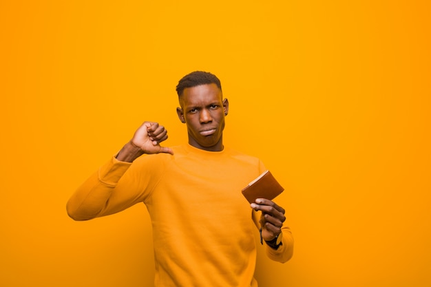 Giovane uomo di colore afroamericano contro la parete arancio, concetto dei soldi.