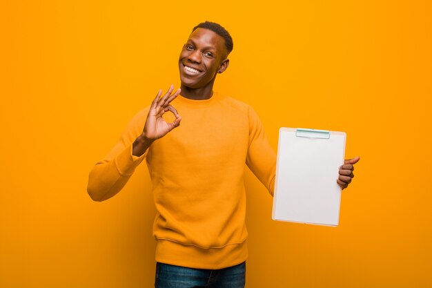 Young african american black man against orange wall wholding a placard