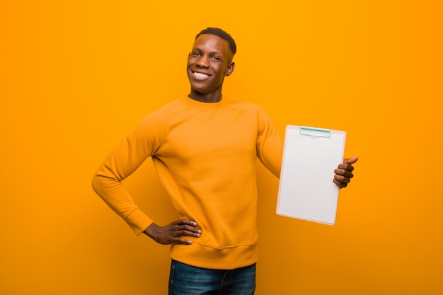 Young african american black man against orange wall wholding a placard