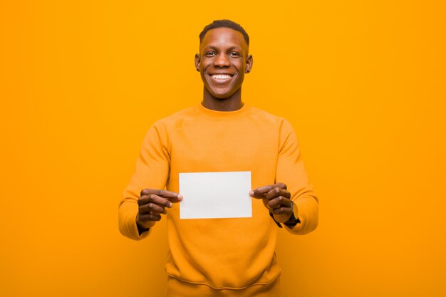 Young african american black man against orange wall wholding a placard