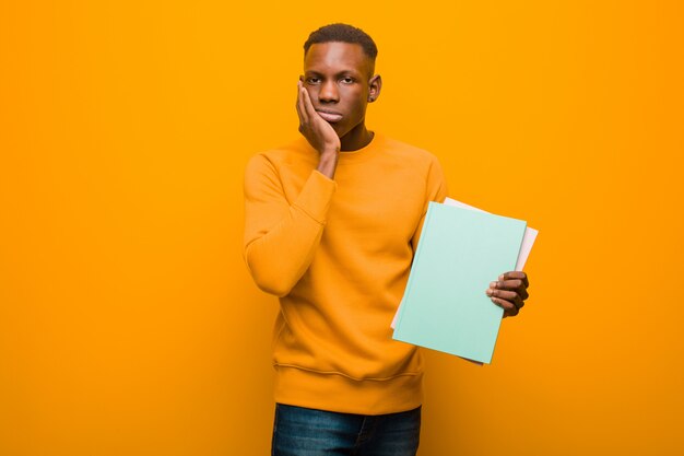 Young african american black man against orange wall with a book