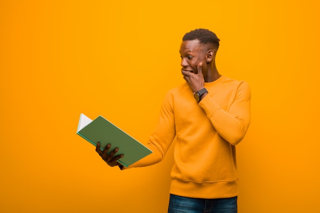 Young african american black man against orange wall with a book