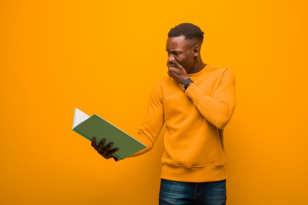 Giovane uomo di colore afroamericano contro la parete arancio con un libro