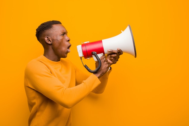 Young african american black man against orange wall with a megaphone