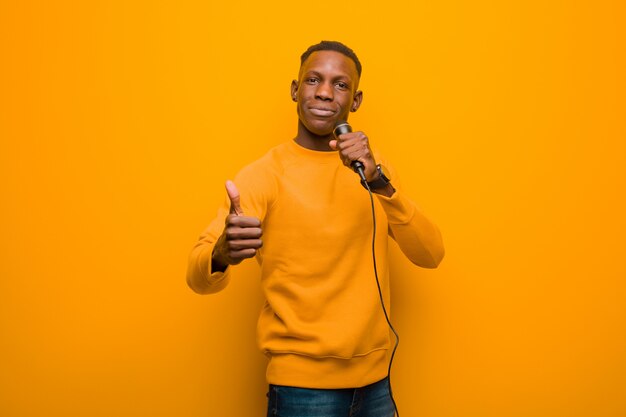 Young african american black man against orange wall with a microphone