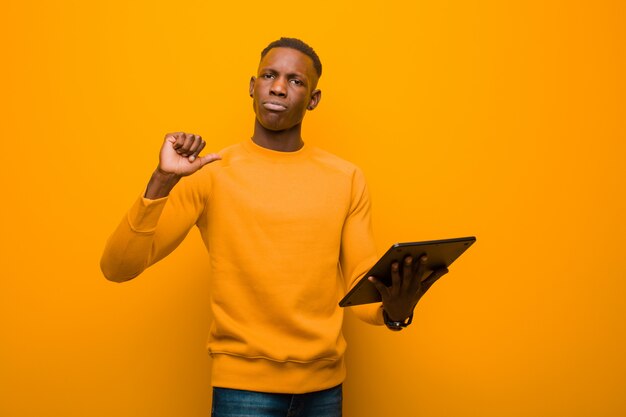 Young african american black man against orange wall with a smart tablet