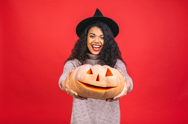 young african american black woman holding a carved pumpkin isolated over red background