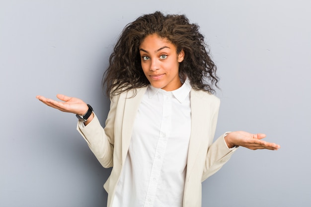 Young african american business woman doubting and shrugging shoulders in questioning gesture.