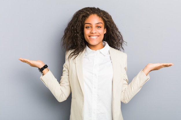 Young african american business woman makes scale with arms, feels happy and confident.