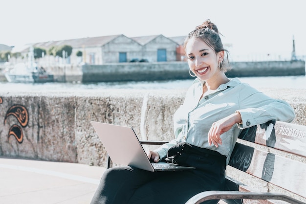 Young african american Businesswoman sitting on a bench at the shore outdoors working on laptop during the rest.Successful freelancer typing on keyboard using laptop computer.Portrait woman copywriter