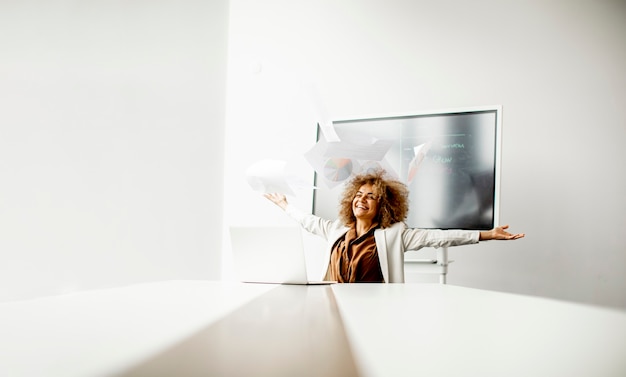 Photo young african american businesswoman throwing paper in the air after receiving of great news in the modern office