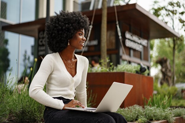 Young african american businesswoman working using laptop sitting on the bench in the city