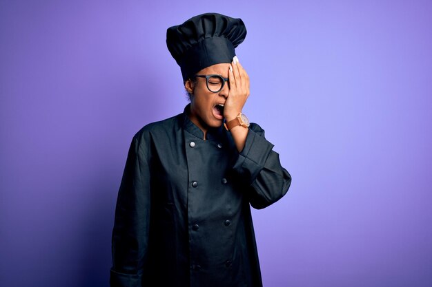 Young african american chef girl wearing cooker uniform and hat over purple background yawning tired covering half face eye and mouth with hand face hurts in pain