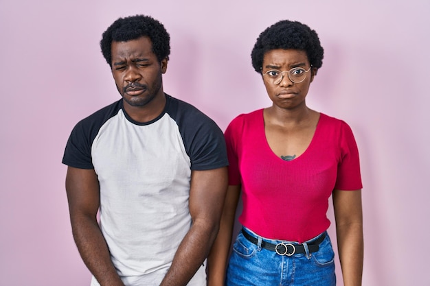 분홍색 배경 위에 서 있는 젊은 아프리카계 미국인 커플은 우울하고 분노하고 두려워하는 슬픈 표정으로 울고 있는 고통에 대해 걱정하고 있습니다.