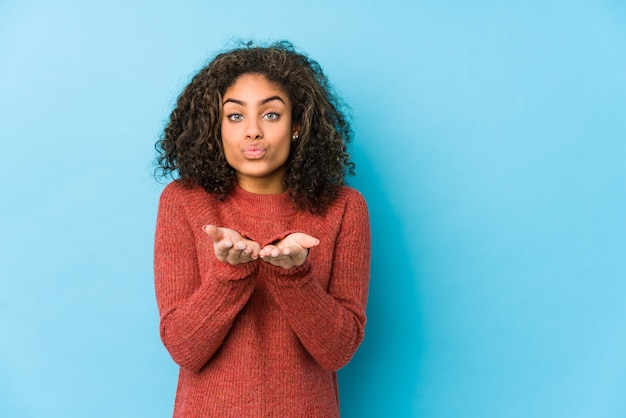 Young african american curly hair woman folding lips and holding palms to send air kiss.