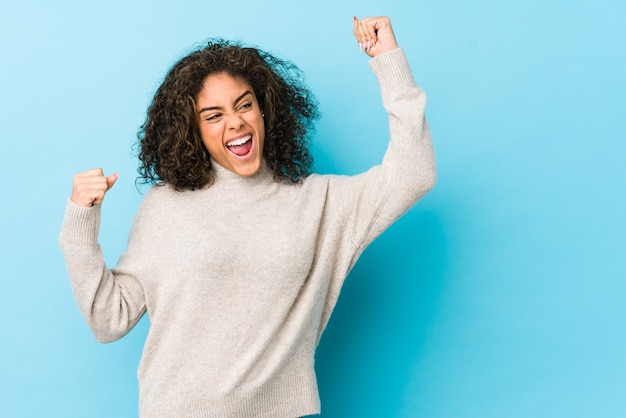 Young african american curly hair woman raising fist after a victory, winner concept.