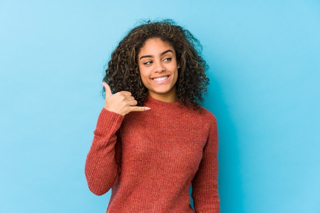 Young african american curly hair woman showing a mobile phone call gesture with fingers.