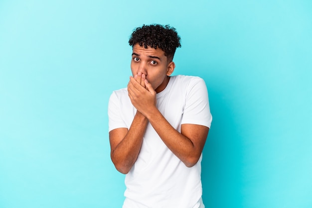 Young african american curly man isolated on blue covering mouth with hands looking worried.