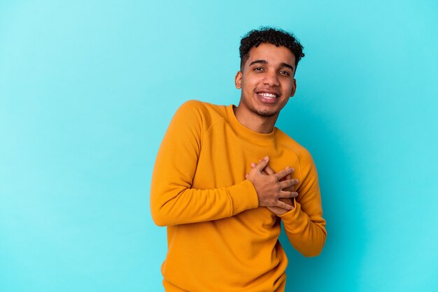 Young african american curly man isolated on blue has friendly expression, pressing palm to chest. Love concept.