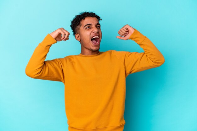 Young african american curly man isolated on blue raising fist after a victory, winner concept.