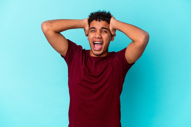 Young african american curly man isolated on blue screaming with rage.