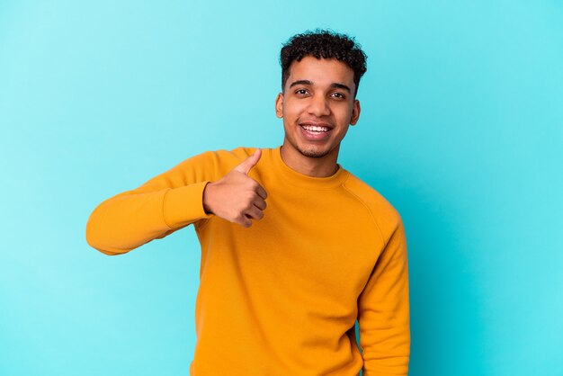 Young african american curly man isolated on blue smiling and raising thumb up