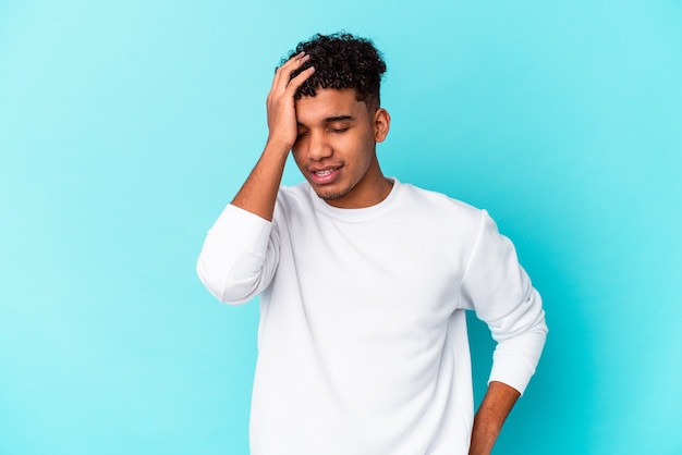 Young african american curly man isolated on blue tired and very sleepy keeping hand on head.