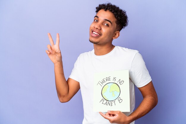 Young african american curly man isolated holding a theres is no planet b poster joyful and carefree showing a peace symbol with fingers.