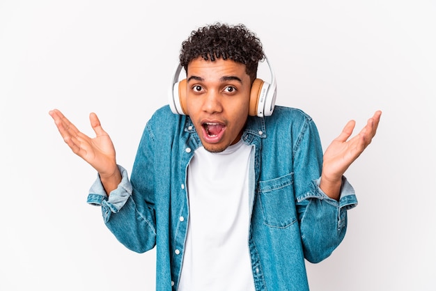 Young african american curly man isolated listening to music with headphones surprised and shocked.