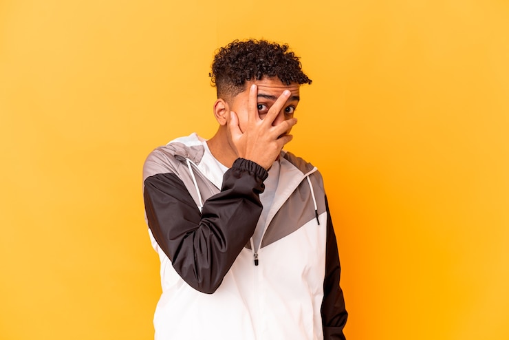 Photo young african american curly man isolated on purple blink through fingers frightened and nervous.