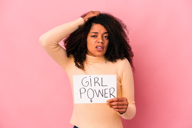 Young african american curly woman holding a girl power message on a placard being shocked, she has remembered important meeting.