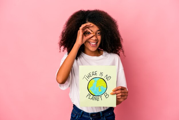 Young african american curly woman holding a planet message on a placard excited keeping ok gesture on eye.