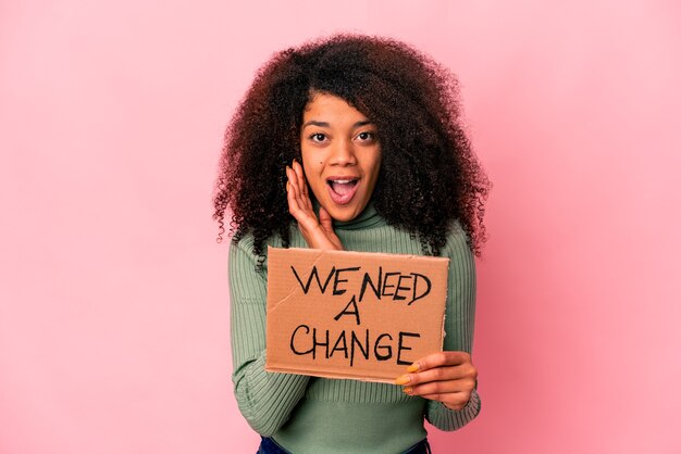 Young african american curly woman holding a we need a change cardboard surprised and shocked.