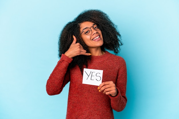 Молодая афро-американская фигурная женщина, держащая плакат «Да», показывающая жест звонка по мобильному телефону с пальцами.