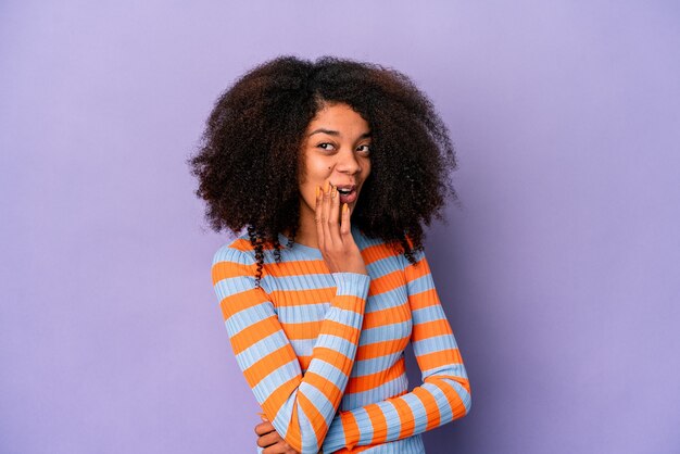 Young african american curly woman isolated on purple background is saying a secret hot braking news and looking aside