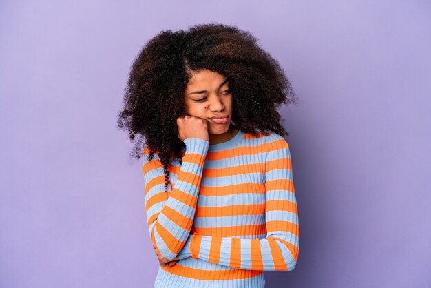 Young african american curly woman isolated on purple background who feels sad and pensive, looking at copy space.