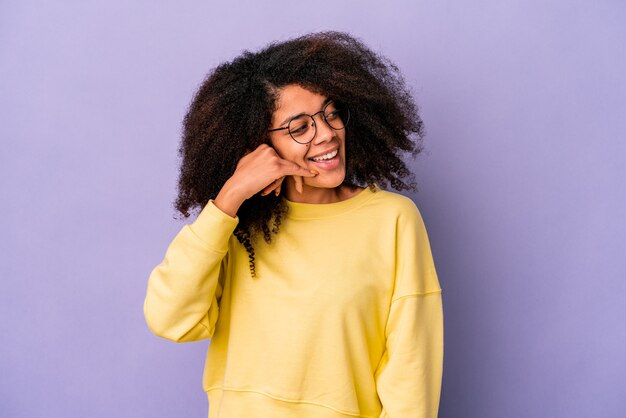 Young african american curly woman isolated on purple wall, showing a mobile phone call gesture with fingers.