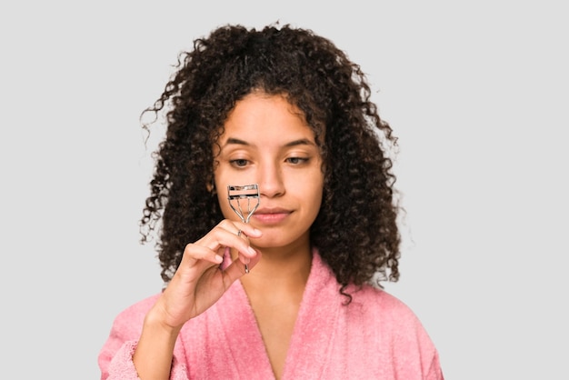 Young african american curly woman using an eyelash curler isolated