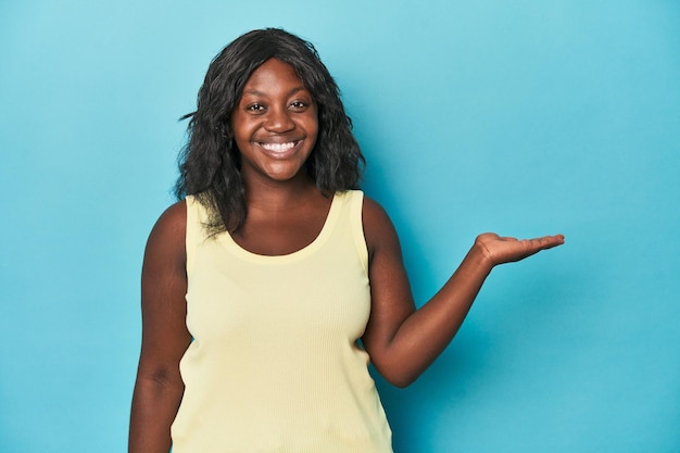 Young african american curvy woman showing a copy space on a palm and holding another hand on waist