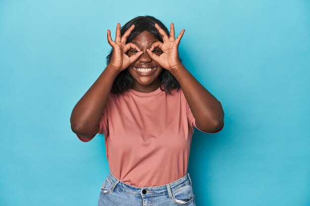 Young african american curvy woman showing okay sign over eyes