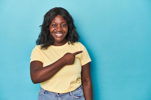 Young african american curvy woman smiling and pointing aside showing something at blank space