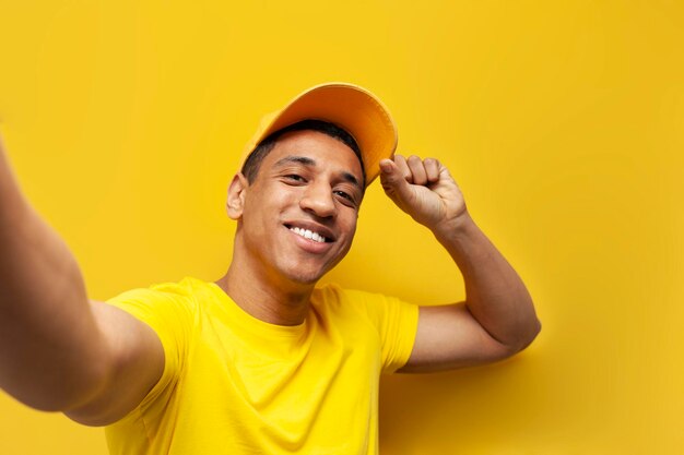 Young african american delivery man in yellow uniform taking selfie on yellow background