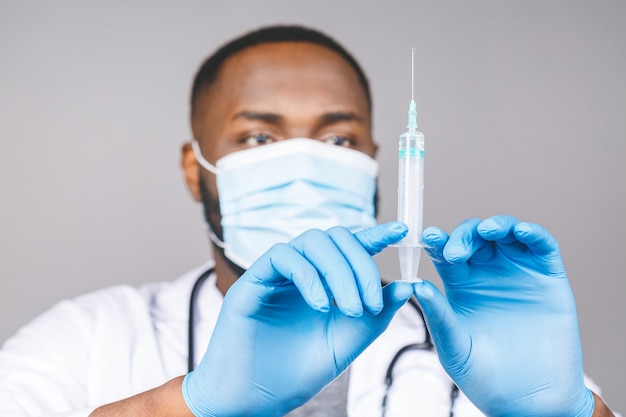 Young african american doctor wearing medical mask and gloves holding syringe with coronavirus vaccine