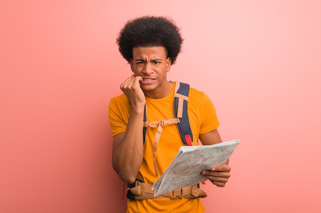 Young african american explorer man holding a map biting nails, nervous and very anxious