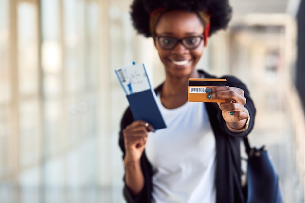 カジュアルな服装の若いアフリカ系アメリカ人女性の乗客は、チケットとクレジットカードを保持している空港にいます。
